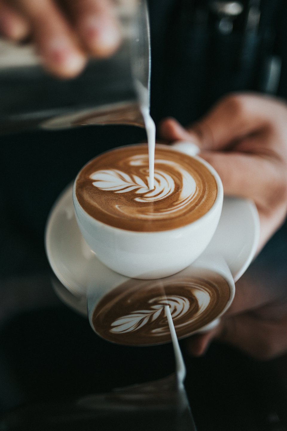 Barista pours steamed milk into espresso, creating leaf latte art.
